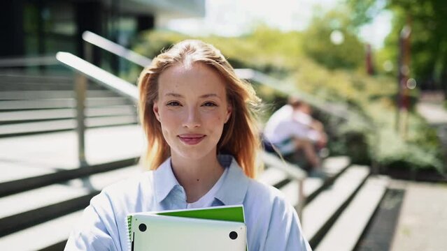 Pretty girl university student holding notebooks looking at camera posing for outdoor portrait. College study programs, academic educational courses ads, learning classes concept.