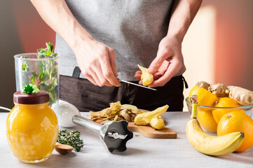 A man peels a ginger. Knife and ginger slices. Prepare a dish with ginger and fruit. Honey, fruits and mint.