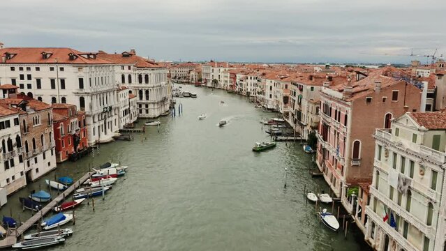 A drone flies over the Grand Canal with empty gondolas parked near the pier, between traditional Italian houses with orange roofs. City on the water from a bird's eye view, Venice, Italy