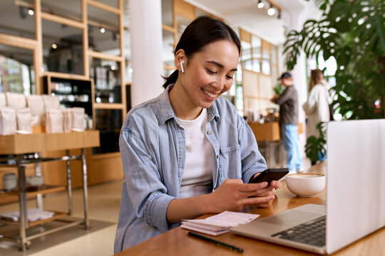 Young smiling Asian woman student using smartphone for elearning wearing earbud, watching online class webinar training in mobile app, studying, having hybrid remote video call on cell phone.
