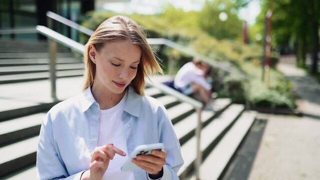 Happy pretty girl university student user holding cell phone using education tech apps looking at smartphone texting messages standing outside. Mobile online applications concept.