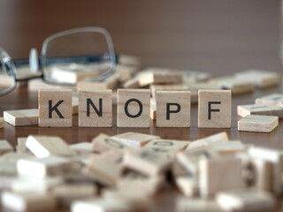 knopf Wort oder Konzept dargestellt durch hölzerne Buchstabenfliesen auf einem Holztisch mit Brille und einem Buch