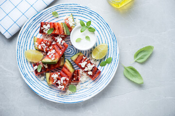 Blue and white plate with grilled watermelon batons, cheese and yogurt, top view on a light-grey stone background, horizontal shot