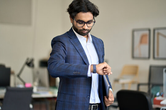 Busy stylish rich indian business man wearing suit looking at watch in office. Businessman checking time waiting for deadline, urgent work, being late, punctuality and time management concept.