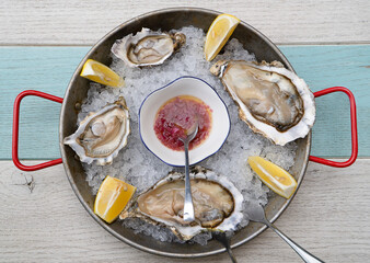 Fresh oysters in a round bowl with ice, lemon and sauce on a wooden table. Shellfish in the...