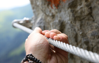 hand holding the steel rope of a via ferrata in the mountains during the hike