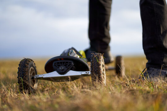 Dirty mountainboard also landboard on green meadow. Human legs in black jeans. Extreme sport art. Gray sky for copy space.