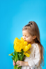 Obraz na płótnie Canvas portrait of a smiling little girl a child with a bouquet of yellow tulips on a blue isolated background. Lifestyle. International Women's or Mother's Day. Space for text. High-quality photography