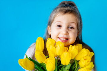 portrait of a smiling little girl a child with a bouquet of yellow tulips on a blue isolated background. Lifestyle. International Women's or Mother's Day. Space for text. High-quality photography