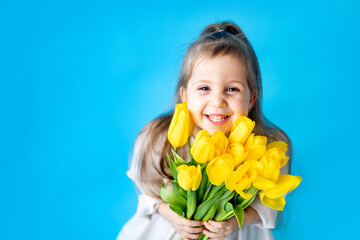 portrait of a smiling little girl a child with a bouquet of yellow tulips on a blue isolated background. Lifestyle. International Women's or Mother's Day. Space for text. High-quality photography