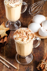 Traditional Christmas drink eggnog and eggs for it cooking on rustic wooden table.