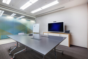 A spacious, bright office meeting room with gray flooring, a glass wall and a large table.