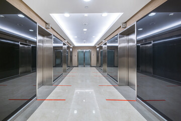 The corridor of an office building with dark glass walls and metal elevator doors. Markings for...