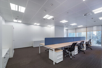 Spacious bright office space with gray carpet, large windows and furniture.