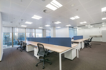 A modern bright office with an open space, with a large window and furniture on a gray carpet.