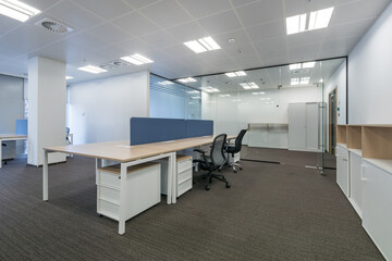 Modern office space with large windows, glass partitions and furniture. Light walls and brown...