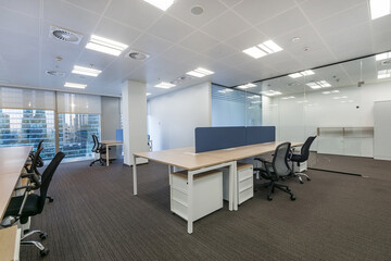 Modern office space with large windows, glass partitions and furniture. Light walls and brown...