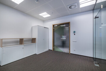 A bright, empty office space with gray flooring, white cabinets and a glass door.