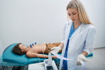 Pediatrician looking ECG printout of child patient after heart electrocardiogram procedure at...