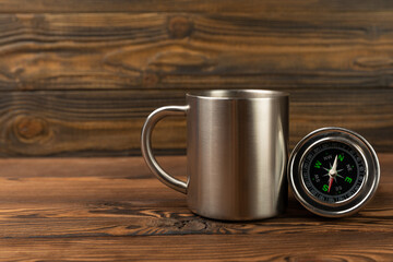 Round compass and travel mug on brown texture background. The concept of tourism with a compass, travel with a compass and outdoor activities with a compass. Travel and vacation.