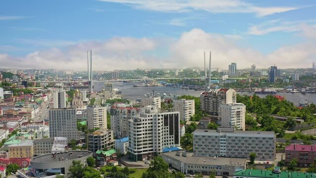 Buildings in the center of Vladivostok from the air. The famous modern Zolotoy Rog Bridge in the sea bay. Cinematic drone movement. The capital of the Russian Far East. A summer sunny day. Stock 4k