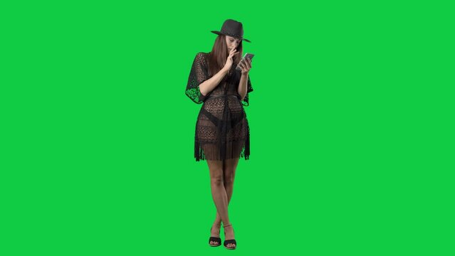 Young busy woman in black bikini and beach tunic using smart phone. Full body isolated on green screen background