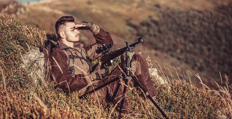 Fotobehang Hunt hunting rifle. Hunter man. Hunting period. Male with a gun. Hunter with hunting gun and hunting form to hunt. Hunter is aiming. Shooter sighting in the target. The man is on the hunt © Yevhen