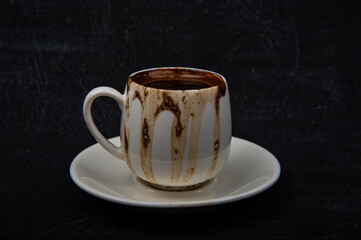 Turkish Coffee in White ceramic cup on black background. Coffee spilled on the rim of the cup.
