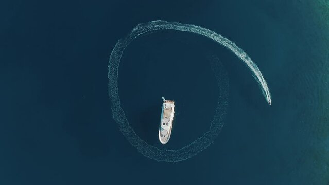 Slow-motion aerial shot fast man with electric surfboard going around his luxury yacht in the circle and making beautiful shapes in the clear sea. Top travel destination. 4K