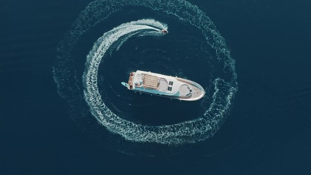 Young adventurous man with electric surfboard hydrofoil going around his luxury yacht in the circle and making beautiful shapes in the clear ocean. Hot summer day, enjoying water sport. Luxury holiday