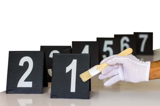 Close-up of a white glove holding a brush against a number plate placed on a table.