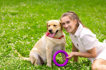a young girl plays with a toy ring with a labrador dog on the grass