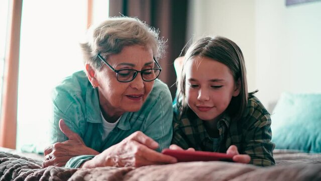 Happy grandmother and her granddaughter using a cellphone together, playing a game. A senior woman and a child girl are having fun.
