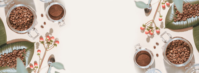 Coffee banner with organic roasted coffee beans on a green leaves and coffee powder in a glass jar on an ivory background with shadows and copy space. Coffee making concept. Flat lay, Banner size