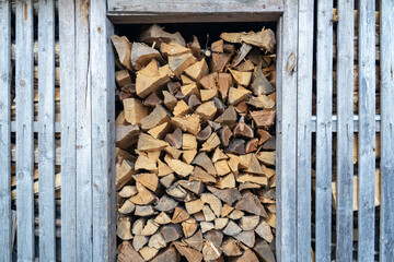 A fragment of the wall of a woodshed made of gray unfinished boards. A pile of firewood is visible through the doorway and a crack in the wall. Background. Texture
