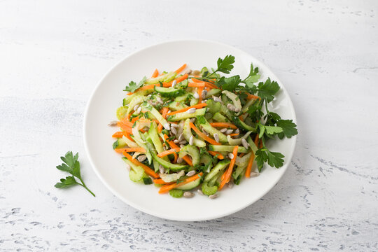A plate with a salad of cucumbers, carrots, celery, seeds and parsley on a light blue background. Delicious healthy homemade food