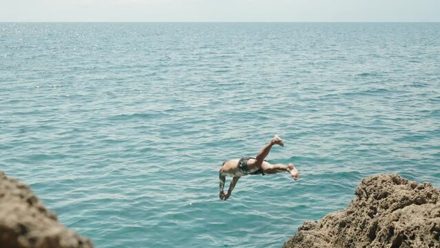 A man in a mask with a tattoo jumps into the sea from a cliff. Slow motion