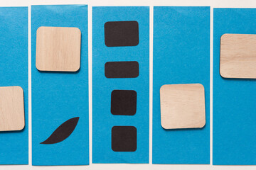 set of wood square tiles with rounded corners and black paper shapes on stripes of blue paper
