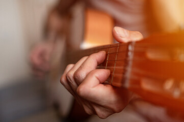 Fototapeta premium male hands of an elderly senior caucasian man holding and playing a classical guitar close up at home. unprofessional faceless guitarist people play amateur music. domestic hobbies and leisure. flare