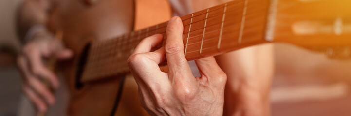 male hands elderly senior caucasian man holding and playing classical guitar close up at home. unprofessional faceless guitarist people play amateur music. domestic hobbies and leisure. banner. flare