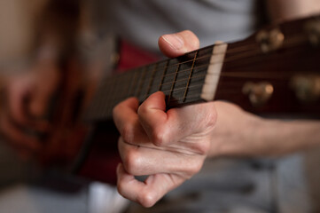 Fototapeta premium male hands of an elderly senior caucasian man holding and playing a classical guitar close up at home. unprofessional faceless guitarist people play amateur music. domestic hobbies and leisure