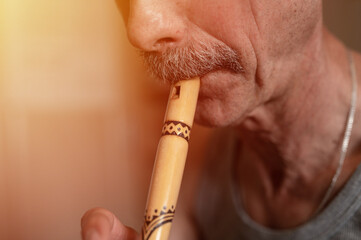 senior man playing the flute. faceless unprofessional male of elderly caucasian recorder people with a moustache with mouth and lips play on pipe amateur music close up at home. hobbies and leisure