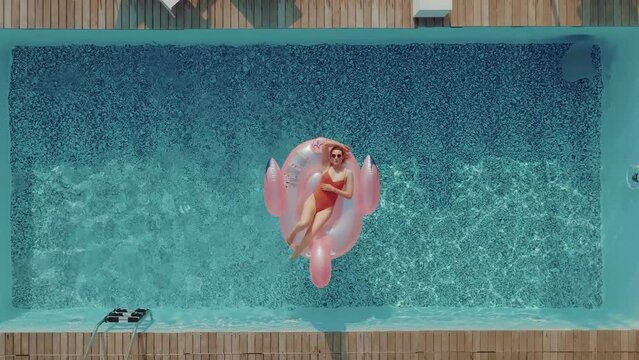 A young woman on vacation is laying on an inflatable pink flamingo in the middle of a swimming pool. Girl relaxing sunbathing enjoying travel holidays at resort pool in bikini. 