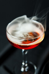 Alcoholic drink. A cocktail with whiskey or cognac with fire and smoke close-up, dark black background. Concept of elite alcohol and nightlife