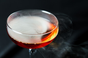 Alcoholic drink. A cocktail with whiskey or cognac with fire and smoke close-up, dark black background. Concept of elite alcohol and nightlife