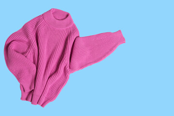 Pink knitted sweater, sleeves to the side, as if indicating an advertisement, concept, on a blue background