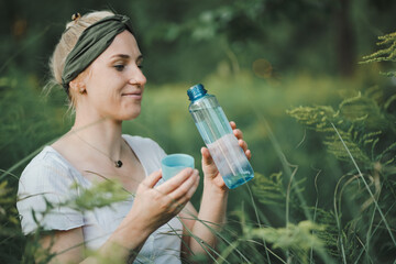 happy young blond alternative looking woman or hippie drinking fresh detox water from a blue...
