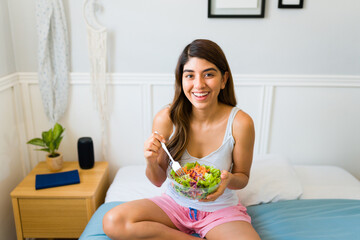 Portrait of a cheerful woman enjoying a healthy salad in bed