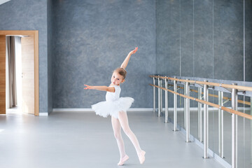 Little ballerina dancing in ballet studio. Cute child girl in white ballet shoes, dress, tutu skirt in class room. Kid in classical dance school for children. Small dancer doing exercises by barre.