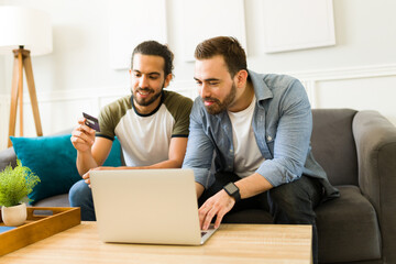 Gay couple doing online shopping on the laptop paying with a credit card